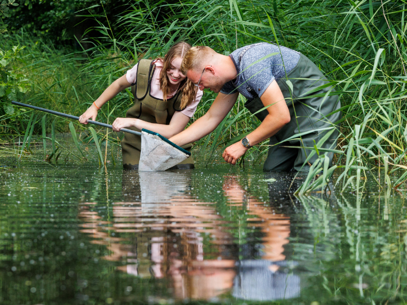 Twee studenten staan in een sloot met een schepnet en doen een veldonderzoek