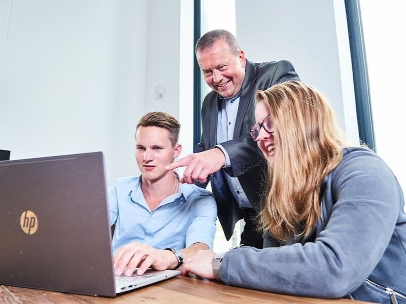 Net geklede studenten zitten achter laptop en krijgen uitleg van professional uit het bedrijfsleven