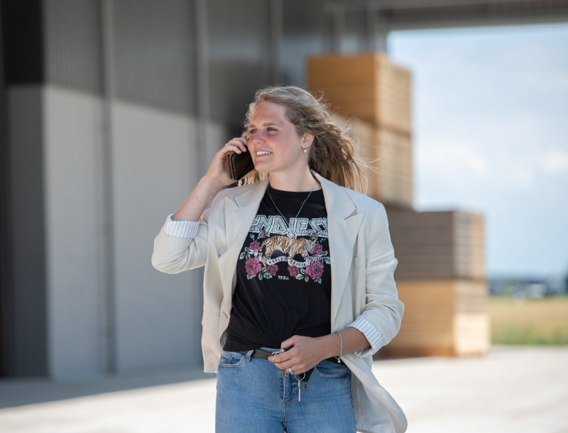 Meisje staat met telefoon aan haar oor te bellen voor kuubskisten bij een agrarisch bedrijf. Coverbeeld van de deeltijd Ad studie Bedrijfskunde en Agrifoodbusiness