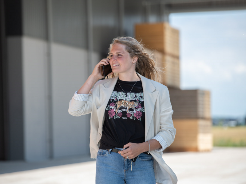 Meisje staat met telefoon aan haar oor te bellen voor kuubskisten bij een agrarisch bedrijf. Coverbeeld van de deeltijd Ad studie Bedrijfskunde en Agrifoodbusiness