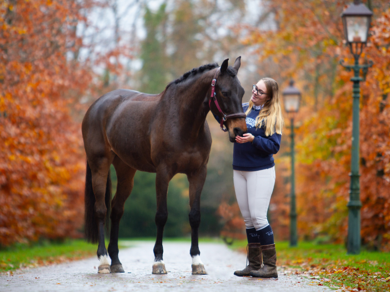 Student Rianne Prins staat met haar paard in het bos in de herfst