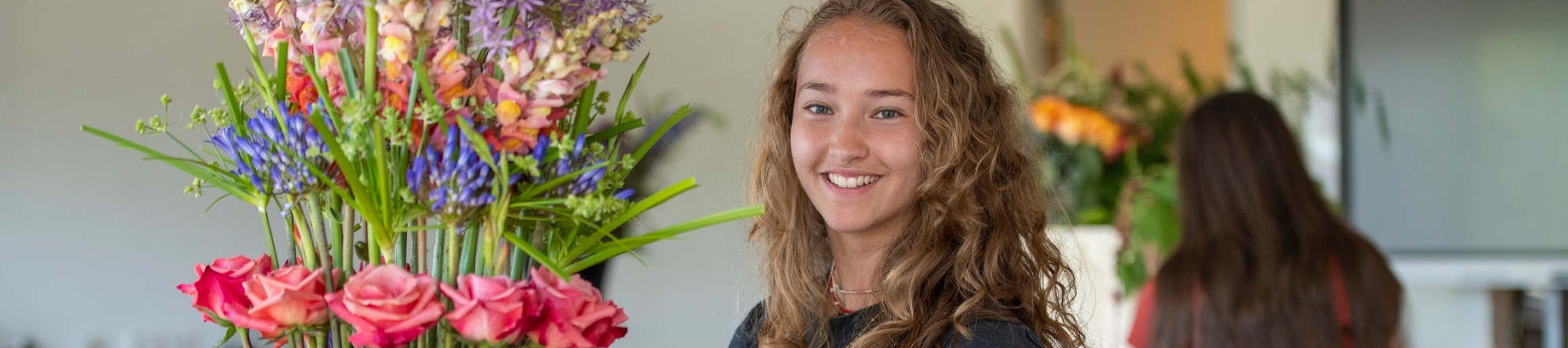 Student bloemsierkusnt met bloemstuk kijkt in de camera en glimlacht